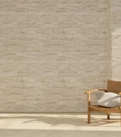 Silla de madera con cojín en un ambiente minimalista, frente a una pared de ladrillos claros y una planta en maceta, iluminado por luz natural.
